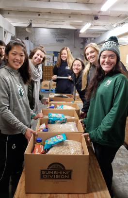 Smiling students stand around boxes of food they have packed for Sunshine Division food pantry