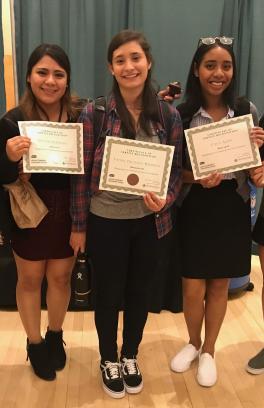 Five students stand facing the camera holding up certificates of service recognition