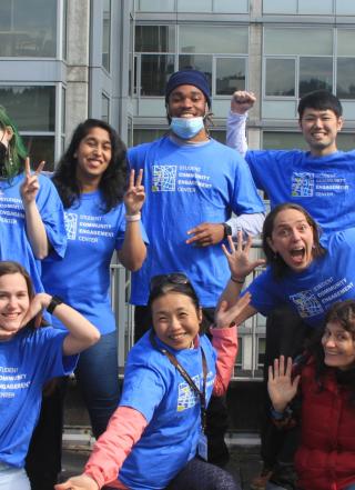 Group of students wearing blue tshirts that say "Student Community Engagement Center" stand together smiling or making funny faces at the camera.