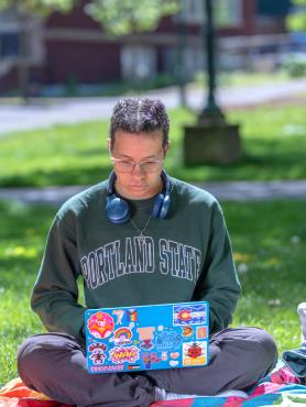 A student working on a laptop sits in the grass in the PSU Park Blocks