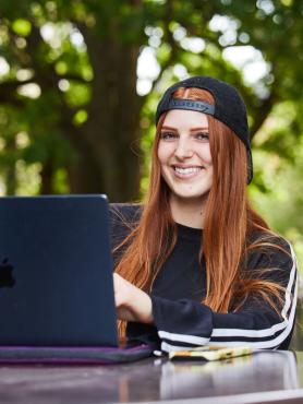 A student working at a laptop at an outdoor cafe table on campus