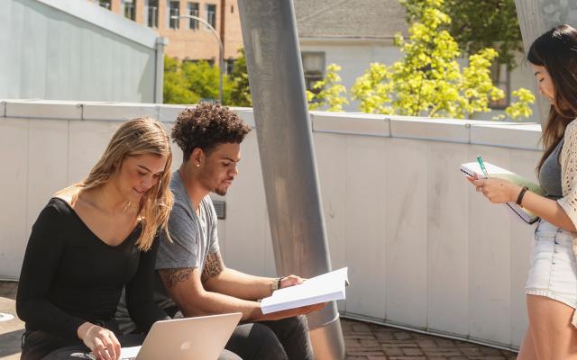 Students sitting outside looking a their computer and books.