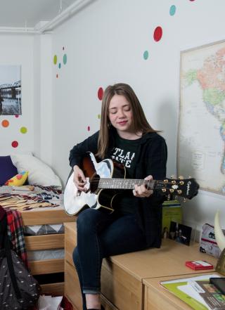 Female student playing guitar in her dorm room