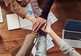 People placing their hands on top of each others in a circle to represent teamwork