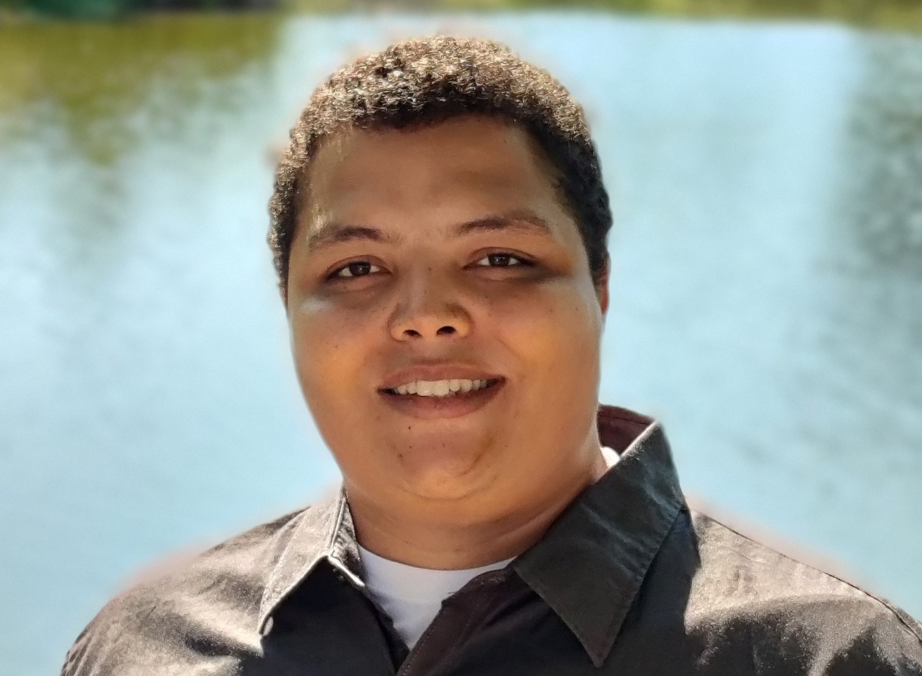 Headshot of Noah, he is facing the camera smiling and there is a body of water behind him