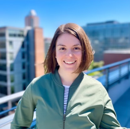 Headshot of Alicia, she is Facing the camera, smiling, on a balcony overlooking the Portland skyline