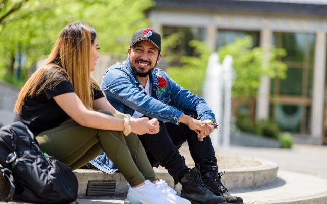 two students sitting outside by water fountain talking