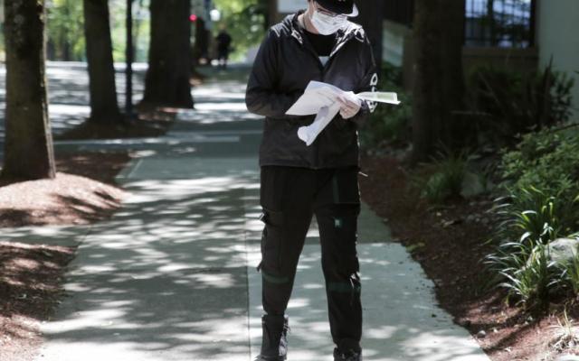 person walking on a sidewalk, looking at a piece of paper