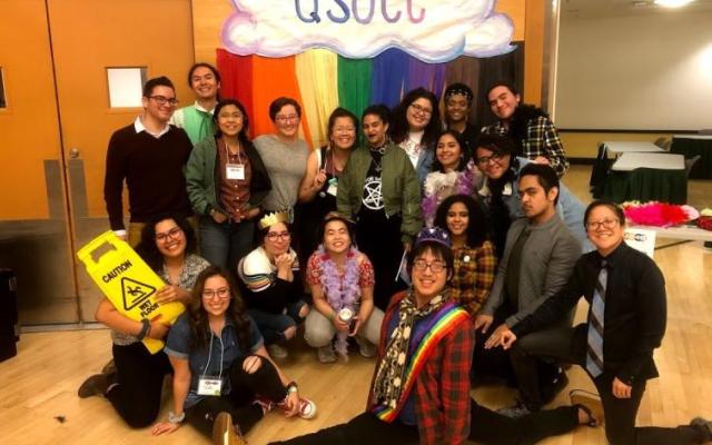 group of people posing in front of a rainbow background