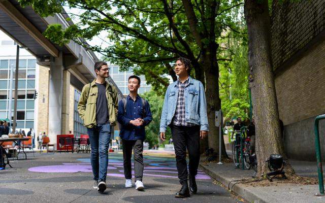 group of three people walking towards the camera with trees framing the street