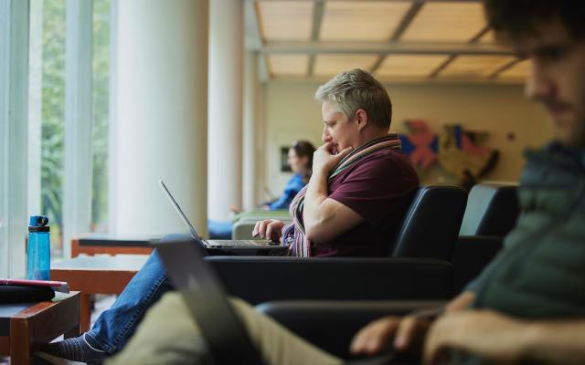 Side view of a student sitting in an armchair using a laptop