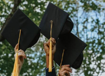 3 hands holding up black graduation caps with gold tassels