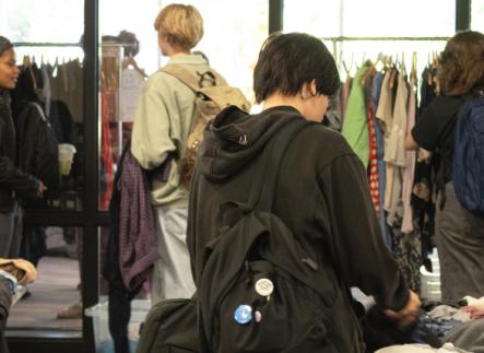4 students browsing clothing racks and tables inside a room