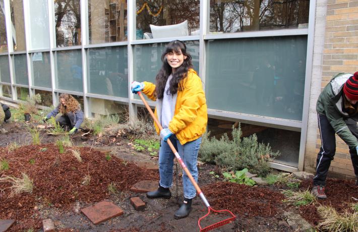 A person in a yellow coat is raking in the garden.