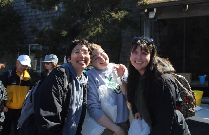 Three students are shown smiling and holding trash bags.