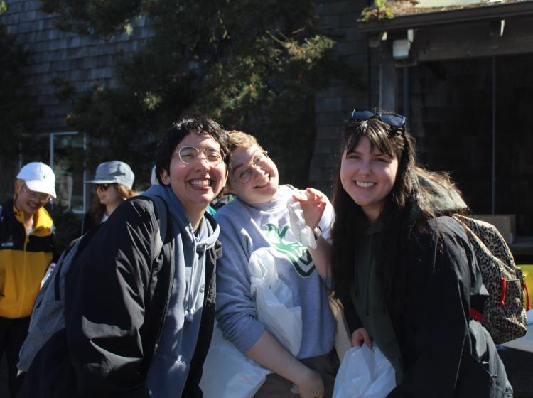Three students are shown smiling and holding trash bags.