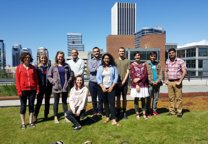 A group of twelve people are standing on a rooftop with the Portland skyline in the background.