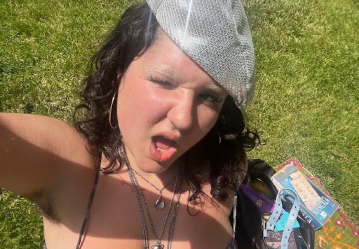 A person with a shiny hat is shown winking with grass in the background.