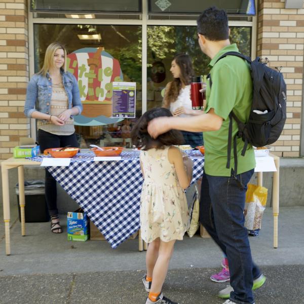 Booth set up outside Little Vikings Childcare, a father and his daughter are walking past.