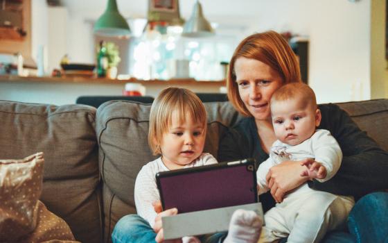 A mother with her two young children on the couch, they're looking at an iPad.