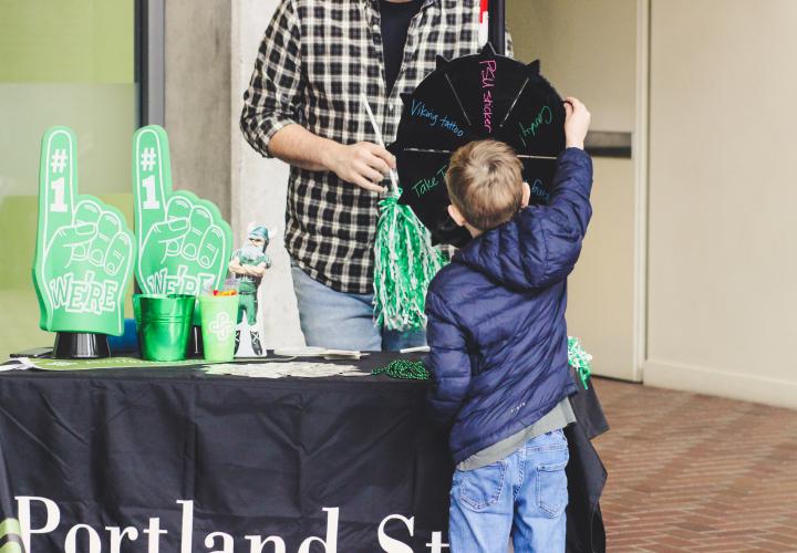 A kid at a Portland State University booth is spinning a prize wheel to see what he wins..