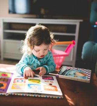 Image of a young child reading a children's book by herself.