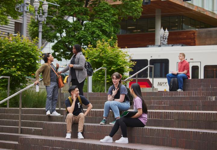 Students chatting on the steps in the Urban Plaza with a MAX train passing