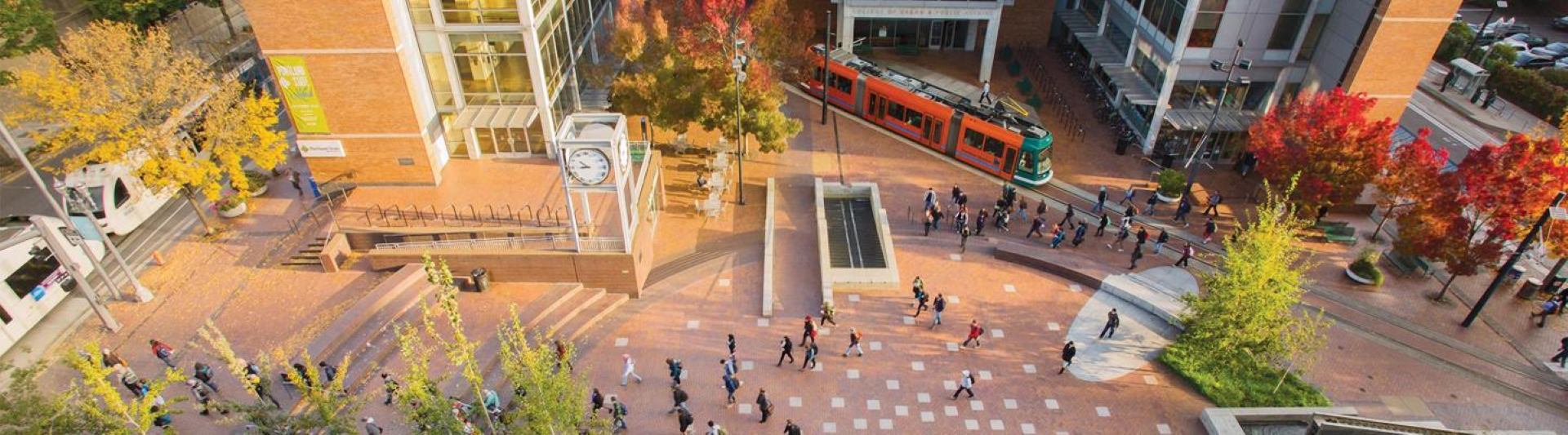 Picture of brick plaza with students, a fountain, a clock tower, tree, and Portland Streetcar
