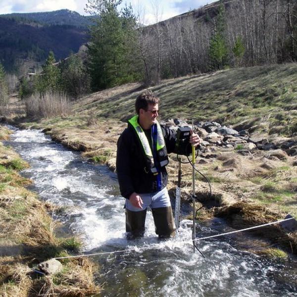 A man stands in a stream holding equipment used to measure the flow of the water