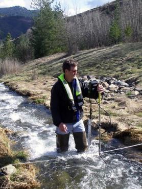 A man stands in a stream holding equipment used to measure the flow of the water