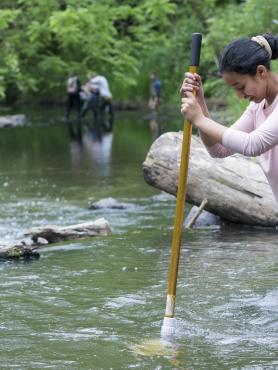 A woman stands in a river measuring the depth of the water