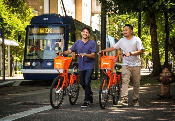 two students walking with orange biketown bike share bicycles