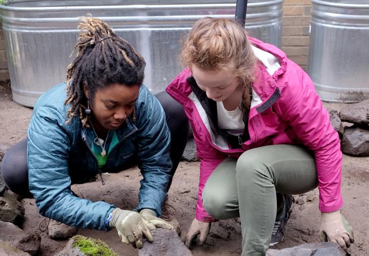 two students moving a rock in a garden