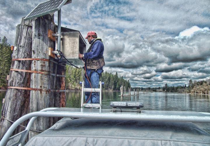 A man stands on a platform in a river building a solar-powered streamgauge