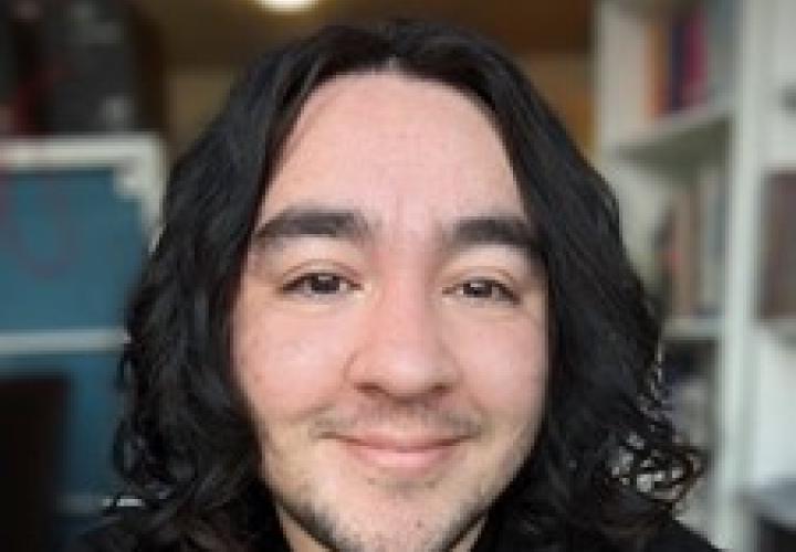 Student with medium-length dark curly hair and a black shirt faces camera smiling