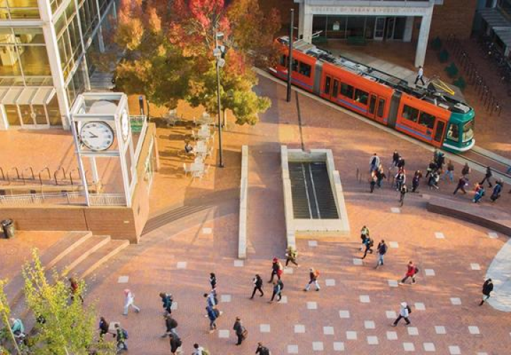 Picture of brick plaza with students, a fountain, a clock tower, tree, and Portland Streetcar