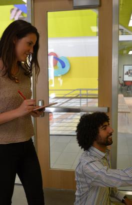 one student standing overlooks and takes notes while another student looks at sensor on the wall