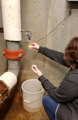 student holds up a collection vile from a spout coming off the side of a large pipe