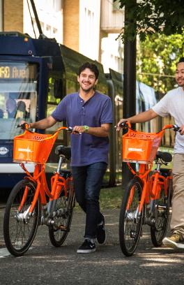 two students walking with orange biketown bike share bicycles