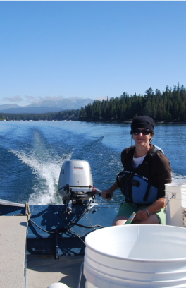 A person driving a motorboat up a river smiles at the camera