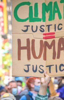 Photo of march with hand holding cardboard sign that is painted to read, "Climate Justice = Human Justice"