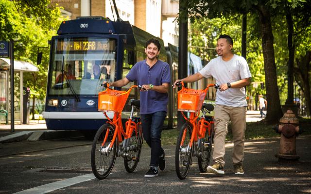 two students walking with orange biketown bike share bicycles