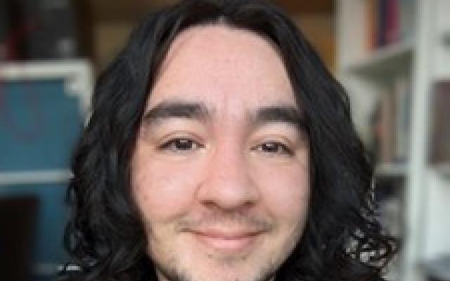 Student with medium-length dark curly hair and a black shirt faces camera smiling