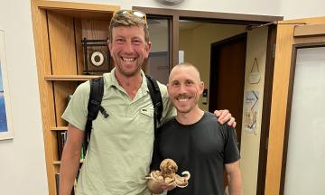 Photo of Fletcher Beaudoin and Paul Loikith standing next to each other. Paul is holding a stuffed octopus. 
