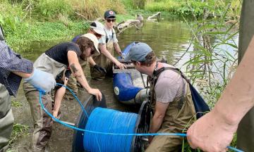 Researchers are setting up water temperature equipment, a long blue cable, in a stream