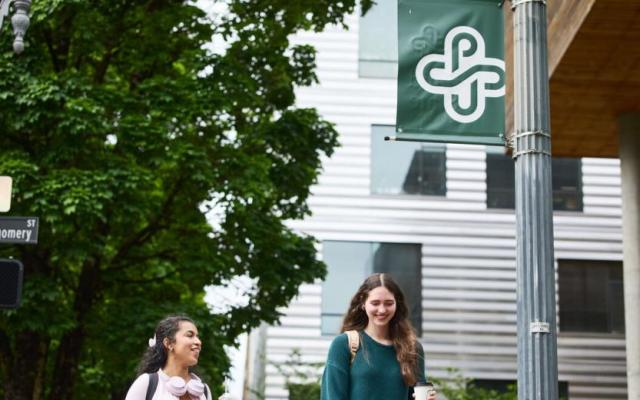 Two PSU students walking together on campus past a Portland State banner