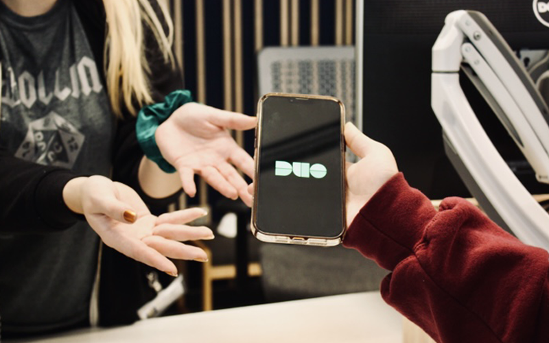 Two OIT employees showcasing a phone that has the DUO secure connection app displayed on its screen.