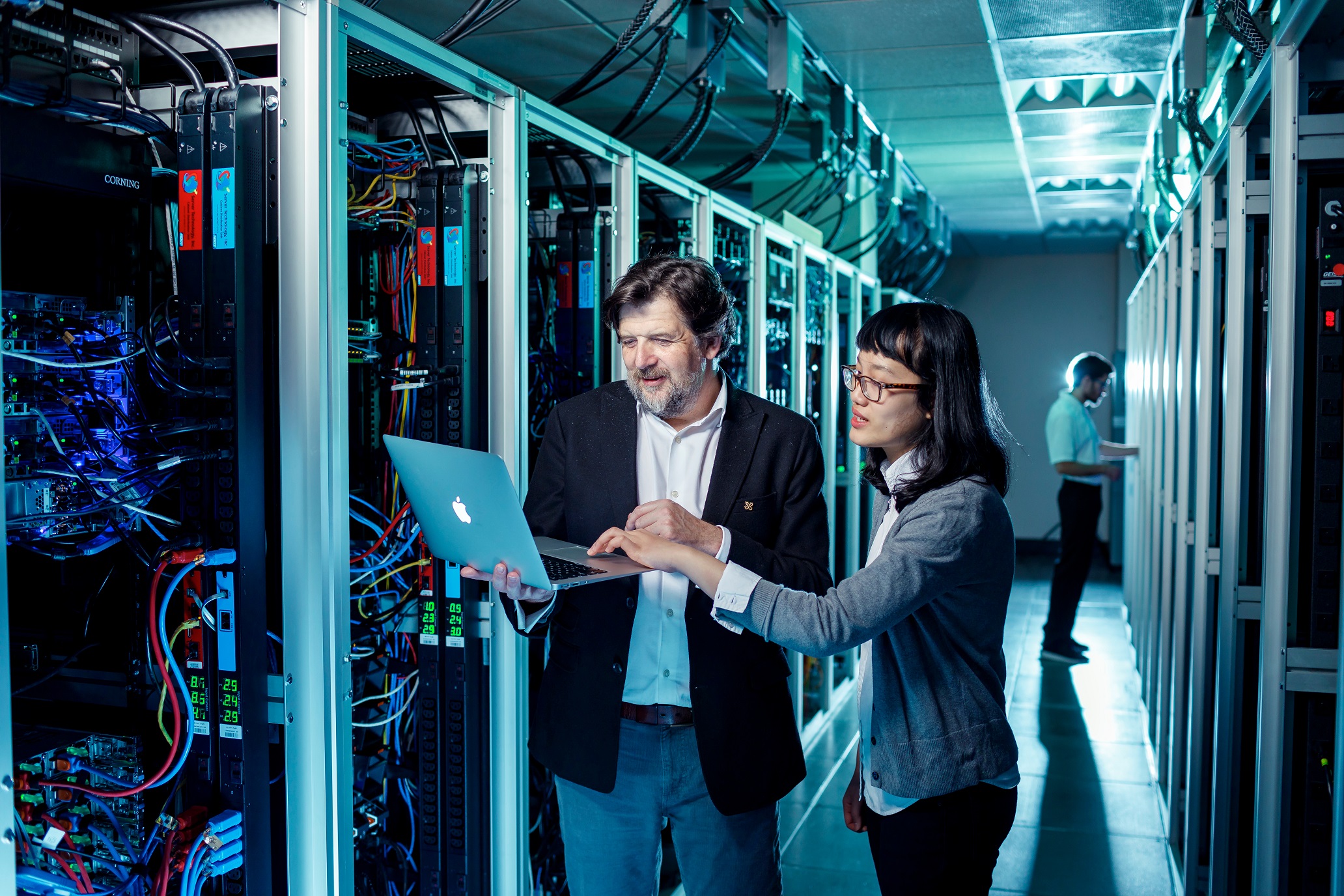 A man and a woman reviewing data on a laptop within a data center
