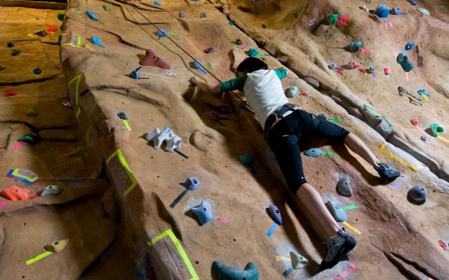 A single person climbing up an indoor rock wall