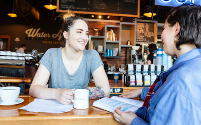 two individuals seated at a coffee shop engaged in conversation